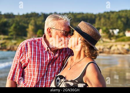 Sanftes Seniorenpaar umarmt und küsst sich an sonnigen Tagen am nassen Ufer des Teiches Stockfoto