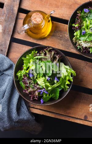 Von oben von leckeren vegetarischen Salat mit grünen und roten Salatblättern und essbaren Blumen gegen Krug Öl Stockfoto