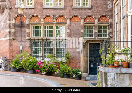 Altes Backsteinhaus mit Metallstangen an Fenstern und Blumenbeeten in der Nähe des Bürgersteiges in Amsterdam Stockfoto