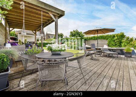 Blumen im Topf auf dem Tisch zwischen Sesseln und Liegestühlen unter dem Sonnenschirm auf der Terrasse von Utrecht Holland Stockfoto