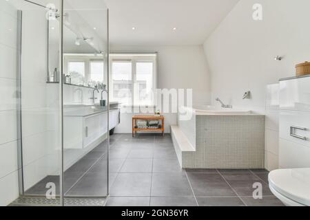 Modernes Badezimmer mit Dusche an der Badewanne und Fenster im Haus mit gefliestem Boden Stockfoto