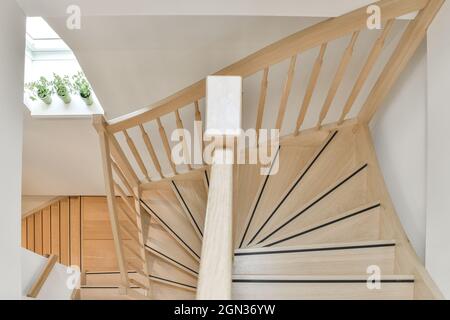 Von oben geschwungene Treppe mit Holzgeländer und Geländer gegen Fensterbank mit Topfpflanzen zu Hause bei Tageslicht Stockfoto