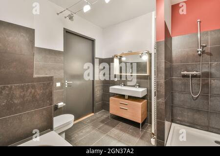 Kombiniertes Badezimmer mit Badewanne, Duschkabine und Waschbecken mit Doppelhähnen und Toilette in der Nähe einer grauen Tür unter glühenden Lichtern Stockfoto