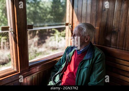 Attraktiver Mann und alter Mann, der in einem alten hölzernen Zugwagen mit Blick aus dem Fenster unterwegs ist Stockfoto