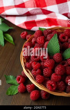 Himbeeren in einer Weidenschale und ein Geschirrtuch auf einem Holztisch. Stockfoto