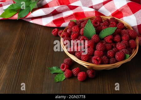 Himbeeren in einer Weidenschale und ein Geschirrtuch auf einem Holztisch. Stockfoto