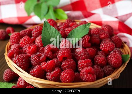 Himbeeren in einer Weidenschale und ein Geschirrtuch auf einem Holztisch. Stockfoto