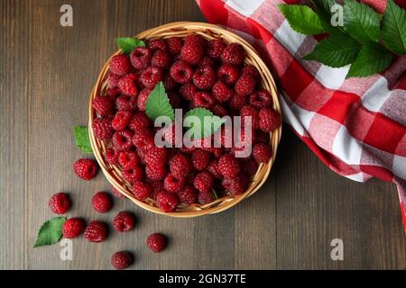 Himbeeren in einer Weidenschale und ein Geschirrtuch auf einem Holztisch. Stockfoto