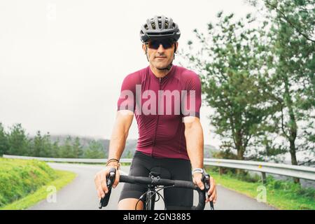 Erwachsene Sportler mit Fahrradsonnenbrille und Helm sitzen auf dem Rennrad auf der Landstraße bei Tageslicht Stockfoto