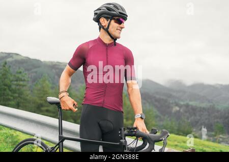 Seitenansicht eines fröhlichen erwachsenen Sportlers in Fahrradsonnenbrille und Helm, der bei Tageslicht auf dem Rennrad auf der Landstraße sitzt Stockfoto