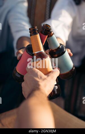 Von oben von Ernte anonyme Freunde klirren Flaschen Bier, während das Wochenende zusammen in der Bar Stockfoto