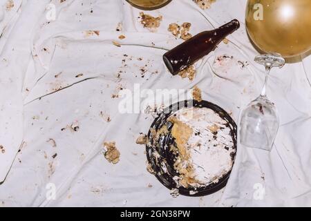 Von oben zertrümmerte Kuchen für die Geburtstagsfeier auf zerbröckelndem schmutzigen Tuch in der Nähe von Luftballons Weinglas und Flaschen auf der Party Stockfoto