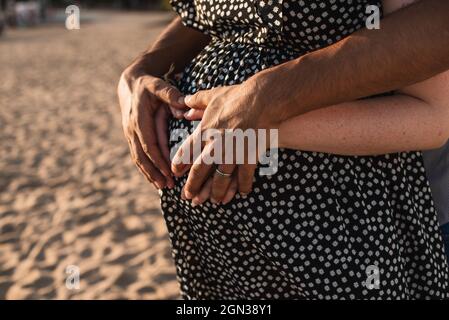 Interracial paar erwartet ein Baby. Herz mit Händen auf dem Bauch der Schwangeren. Stockfoto