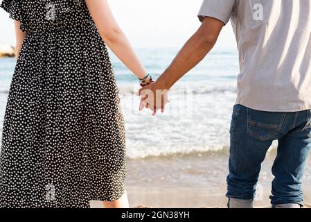 Interrassisches Paar, das die Hände vor dem Meer hält Stockfoto