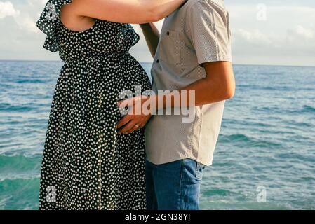Eine Schwangerin umarmte ihren Partner am Meer. Interracial paar mit schwanger erwarten ein Baby. Stockfoto
