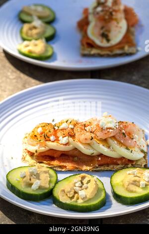 Scandinavian Style Open Sandwich Roggen Knäckebrot Geräucherter Lachs In Scheiben Geschnittenes Gekochtes Ei Garnelen Feta-Käse Und Paprika Gurkenscheiben Mit Hummus Stockfoto