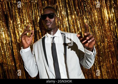 Cooler afroamerikanischer Mann in Jacke und Krawatte tanzt gegen Lametta, während er Silvester feiert Stockfoto