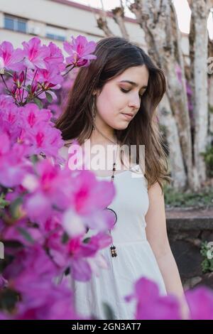 Sanfte Teenager mit braunem Haar in Perlen gegen blühende violette Blumen im Stadtpark Stockfoto