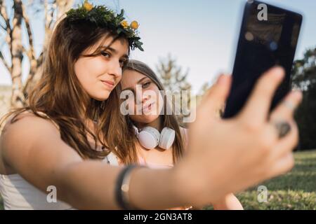 Weibliche Teenager, die sich auf dem Handy im sonnigen Park auf unscharfem Hintergrund porträtieren Stockfoto