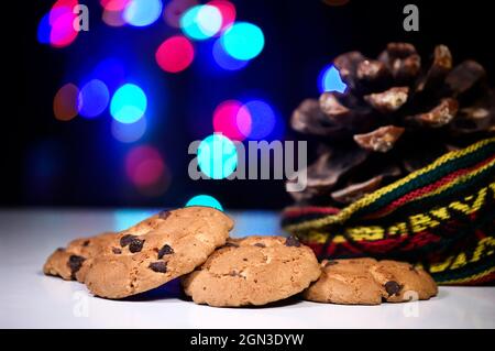 Handgemachte Kekse mit Schokoladenstückchen und Weihnachtsbeleuchtung im Hintergrund. Stockfoto