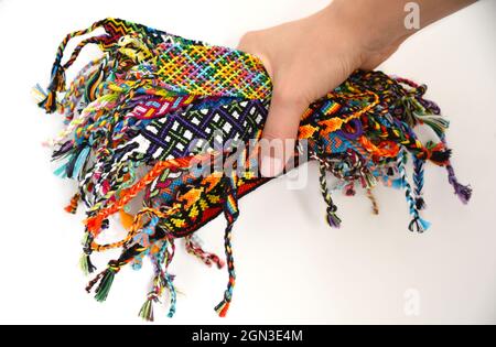 Weibliche Hand hält viele gewebte mehrfarbige DIY Freundschaft Armbänder handgefertigt von Stickerei Thread mit Knoten auf weißem Hintergrund. Stockfoto