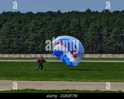 Fallschirmspringer landet auf einer Graspiste, während ein blaues, weißes und rotes Baldachin während einer Flugschau zusammenbricht. Stockfoto