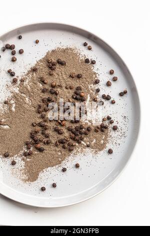 Gemahlen und ganz schwarzer Pfeffer auf runder Platte Stockfoto