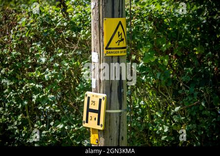 Warnschild Todesgefahr und Hydrantenanzeige H auf einem Holzmast gegen eine gemischte grüne Hecke Stockfoto