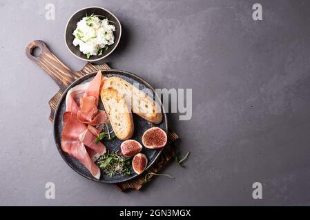 Teller mit Prosciutto Antipasto, Toast, Ricotta auf einem Schneidebrett auf einem grauen Hintergrund, Schinken-Snack, Kopierplatz. Stockfoto