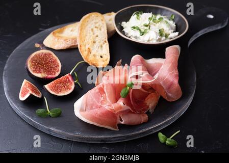 Wurstplatte mit Prosciutto, Käse, Brotscheiben und Feigen auf schwarzem Hintergrund, Nahaufnahme. Stockfoto