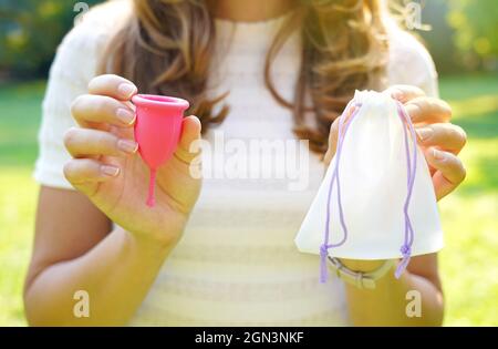 Junge Frau hält eine Menstruationstasse mit Beutel, der vor grünem, natürlichem Hintergrund steht Stockfoto