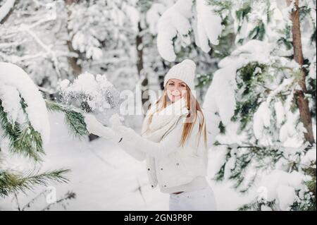 Porträt einer Frau in weißen Kleidern in einem kalten Winterwald. Ein Mädchen mit einem weißen Hut auf dem Kopf in einem schneebedeckten Winterwald Stockfoto