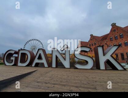 Ein riesiges Danziger Schild vor einem Riesenrad und einem traditionellen Backsteingebäude Stockfoto