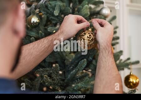 Nahaufnahme eines nicht erkennbaren Mannes, der Dekorationen am Weihnachtsbaum hängt Stockfoto