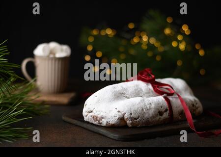 Traditionelles Weihnachtsstollen verzierte Festseil auf einem festlichen Tisch mit Girlande, Kaffeetasse und immergrünen Kiefernzweigen. Weihnachtsfeiertage traditionell Stockfoto