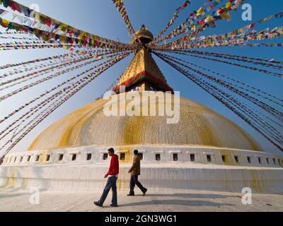 Zwei junge Männer laufen bei Sonnenuntergang in Kathmandu, Nepal, um die Boudhanath-Kuppel herum. Es ist eines der größten Stupas der Welt Stockfoto