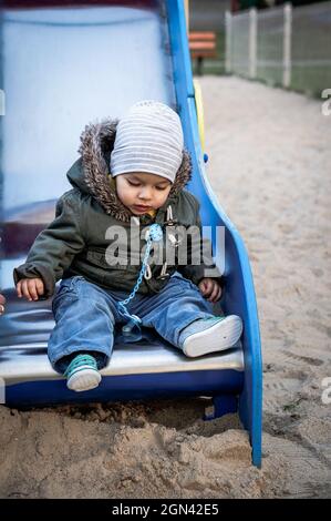 POZNAN, POLEN - 04. Oktober 2016: Ein junger polnischer kaukasischer Kleinkind, der auf dem Boden der Rutschausrüstung auf einem Spielplatz sitzt. Stockfoto