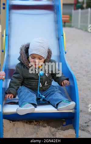 POZNAN, POLEN - 23. Apr 2015: Ein junger polnischer kaukasischer Kleinkind, der auf dem Boden der Rutschausrüstung auf einem Spielplatz sitzt. Stockfoto