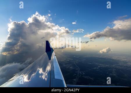 Flugflugzeug des Flügels über dramatischen weißen, flauschigen Wolken am blauen Himmel während des Sonnenuntergangs Stockfoto