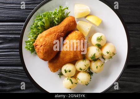 Köstliches knuspriges, frittiertes Huhn mit Zitrone und gekochten Kartoffeln aus der Nähe auf einem Teller auf dem Tisch. Horizontale Ansicht von oben Stockfoto