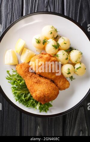 Wiener Backhendl Österreichisches paniertes Fried Chicken mit gekochten Kartoffeln in der Nähe auf dem Teller auf dem Tisch. Vertikale Draufsicht von oben Stockfoto