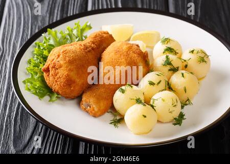 Österreichisches frittiertes paniertes Huhn serviert mit Zitrone und neuen Kartoffeln aus der Nähe auf einem Teller auf dem Tisch. Horizontal Stockfoto