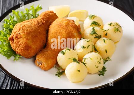 Köstliches knusprig frittiertes Huhn mit Zitrone und gekochten Kartoffeln in der Nähe auf einem Teller auf dem Tisch serviert. Horizontal Stockfoto