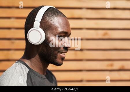 Fröhlicher afrikanischer Sportler, der die Musik in kabellosen Kopfhörern genießt, während er im Freien trainiert Stockfoto