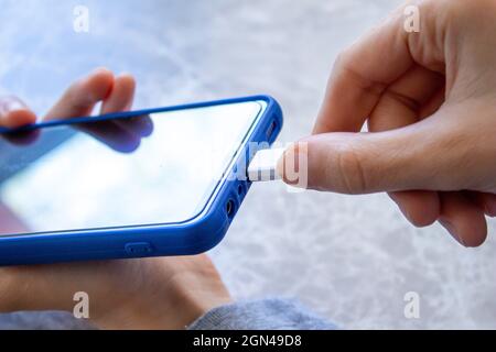 Junge Frau steckt ihr Telefon in das Ladegerät. Stockfoto