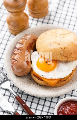 Frühstückssandwich mit Spiegelei, Käse, Wurst auf einem Teller. Frühstück oder Mittagessen im Café, Restaurant Stockfoto
