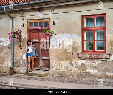 Ein schönes brünett Mädchen steht in der Nähe der alten roten Holztüren eines alten Hauses Stockfoto