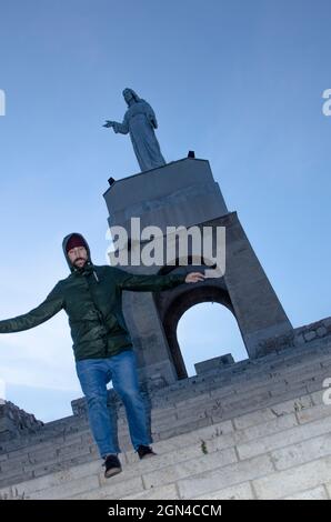 Der junge Mann läuft einige Stufen auf einem Hügel in einer Stadt hinunter, wo oben eine Statue steht Stockfoto