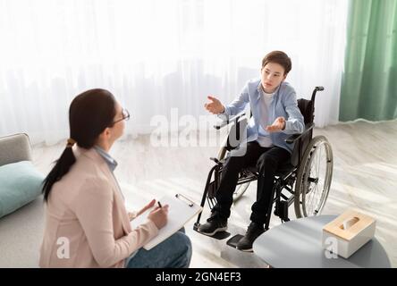 Psychologin, die im Büro einen behinderten Teenager im Rollstuhl konsultiert. Berater, der mit beeinträchtigten Jugendlichen arbeitet, bei psychischen Problemen hilft, aus Stockfoto