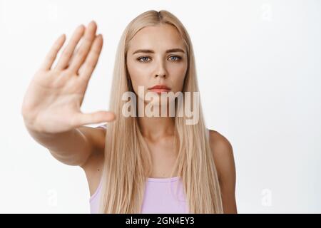 Selbstbewusste junge Frau streckt die Hand aus, um eine Stoppgeste zu zeigen, nein zu sagen, etwas zu verbieten, nein zu sagen, auf weißem Hintergrund zu stehen Stockfoto